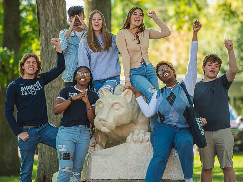 A group of diverse students cheering around the Nittany Lion Shrine